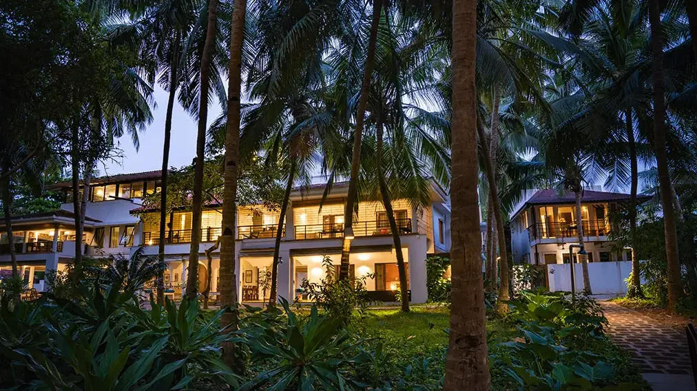 Raht Aashyana Lakhanpal main house glowing at dusk among coconut palms, Candolim, Goa
