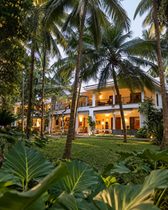 Raht Aashyana Lakhanpal main house glowing at dusk among coconut palms, Candolim, Goa